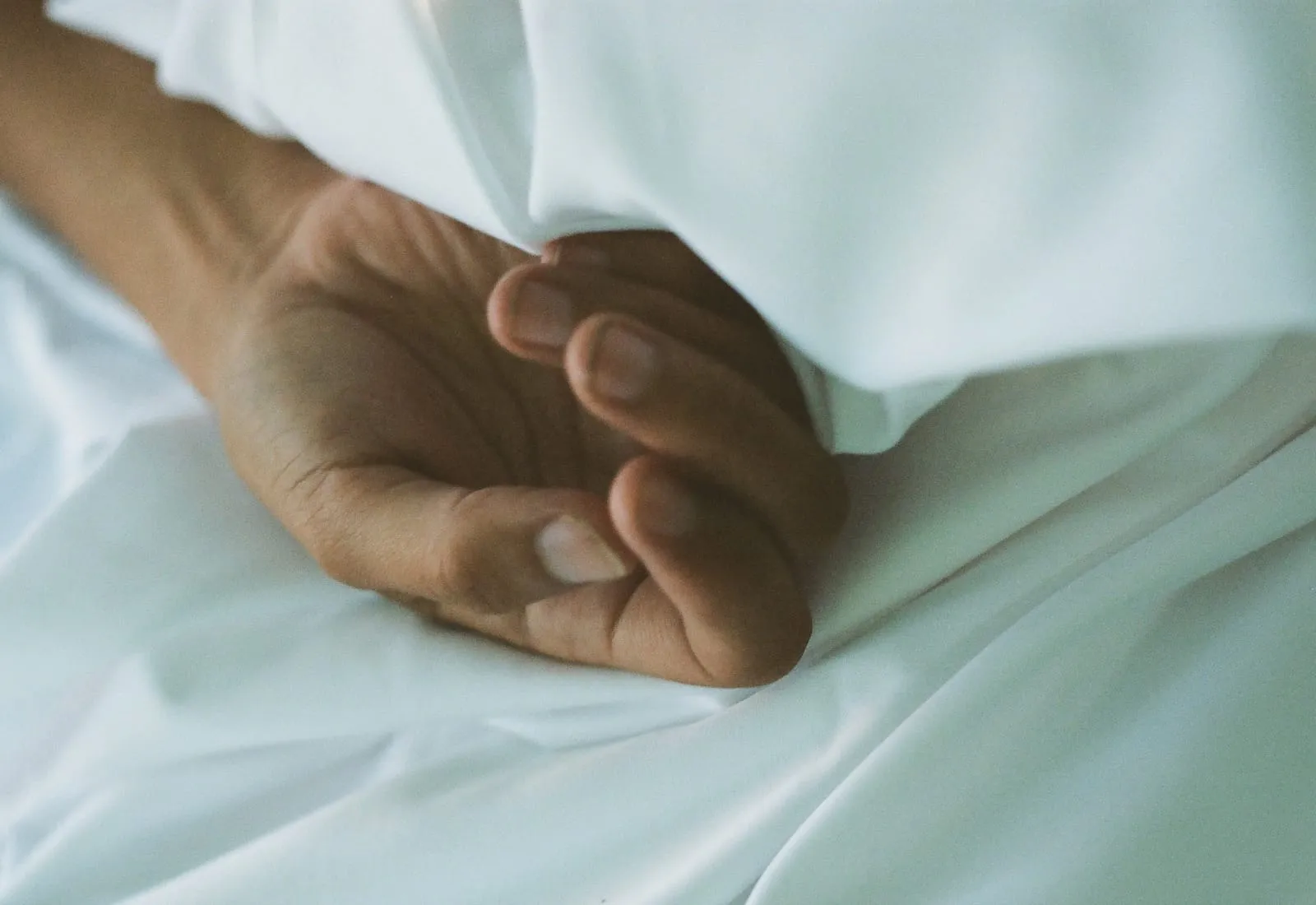 Une main repliée, abandonnée sur le drap blanc