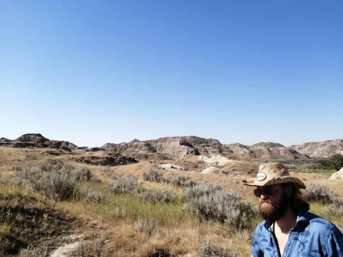 Josh Whelan, chapeau de paille, devant un paysage de badlands et de prairie sèche