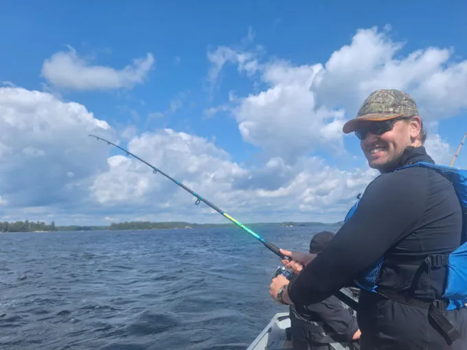Josh Whelan pêchant depuis un bateau, canne à la main, sur un lac par temps clair